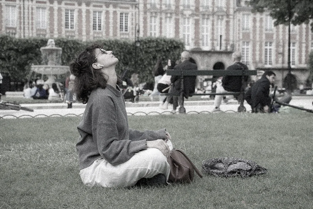 A woman sitting cross-legged on the grass with her head tipped back, laughing