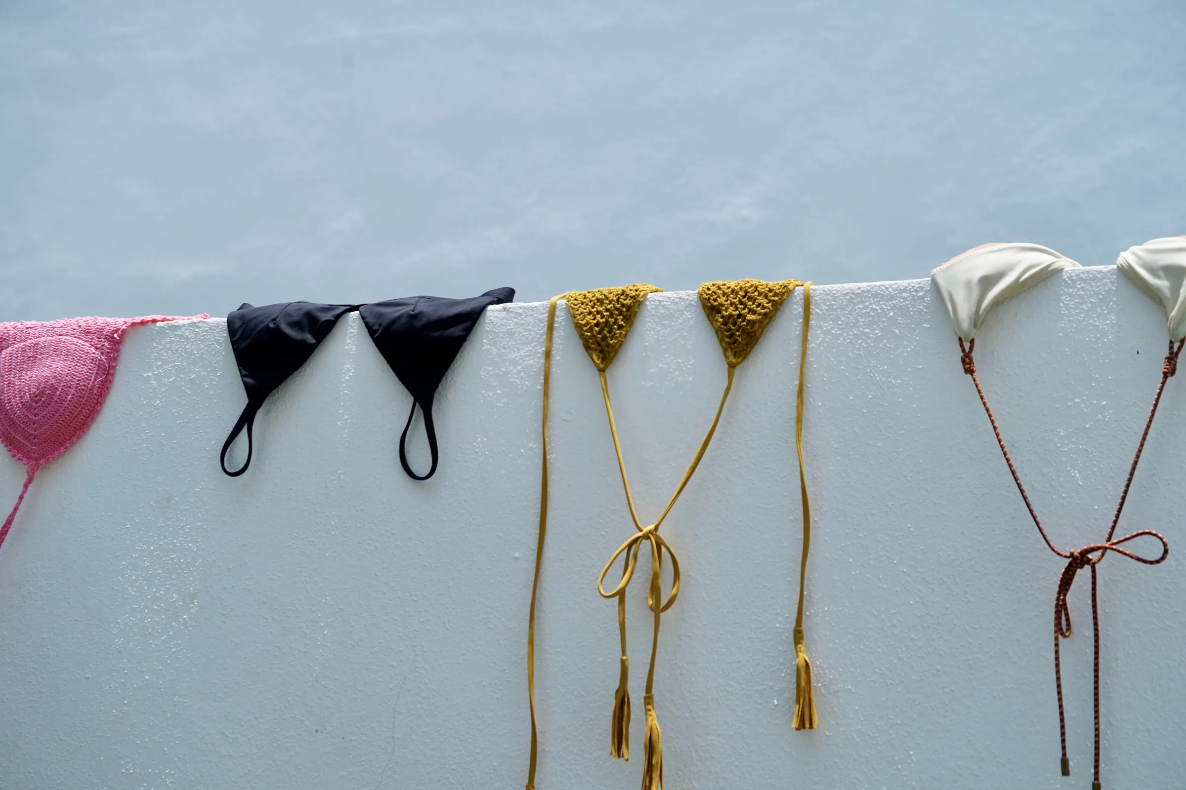 Pink, black, gold and ivory swimwear hanging over a white wall against a blue sky