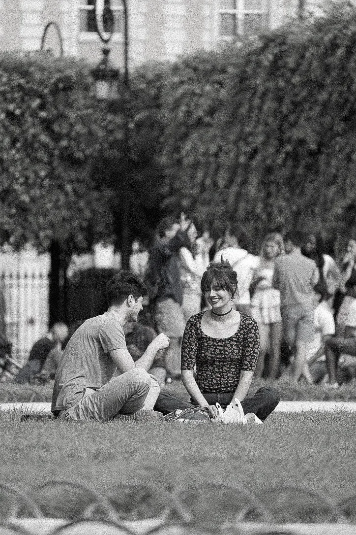 Black and white photograph of a couple sitting on the grass in a Paris park, mid-conversation
